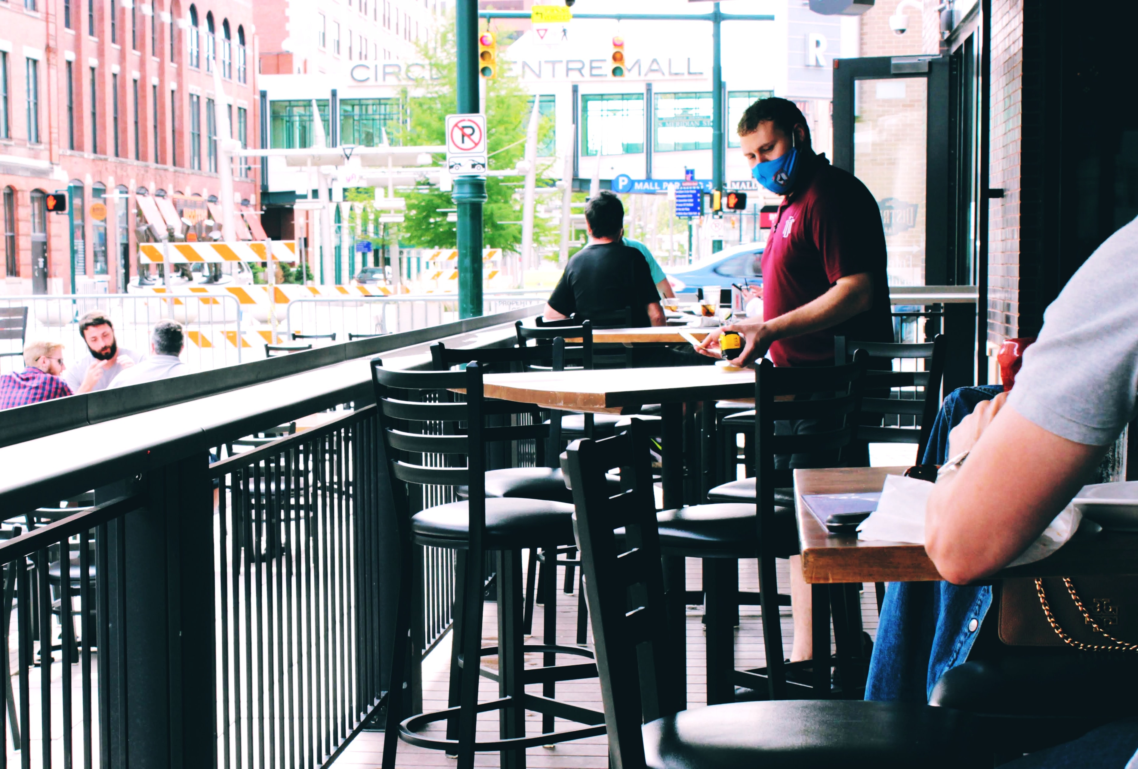 A restaurant worker wearing a mask while cleaning an outdoor table.